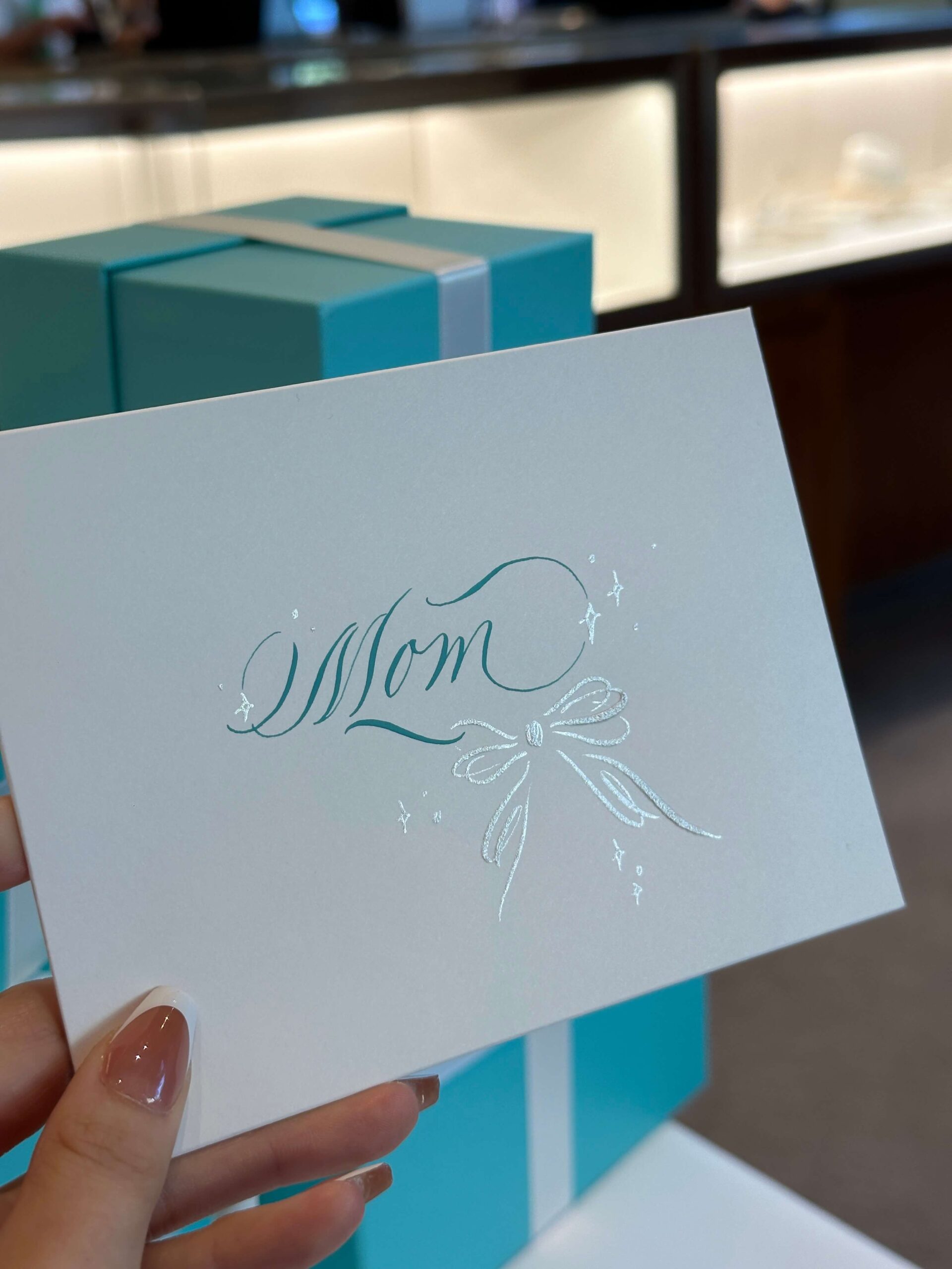 "Mom" written in blue ink calligraphy script with a silver bow.