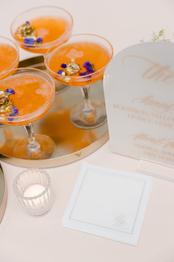 Custom calligraphy monogram on white bar napkins with orange cocktails.