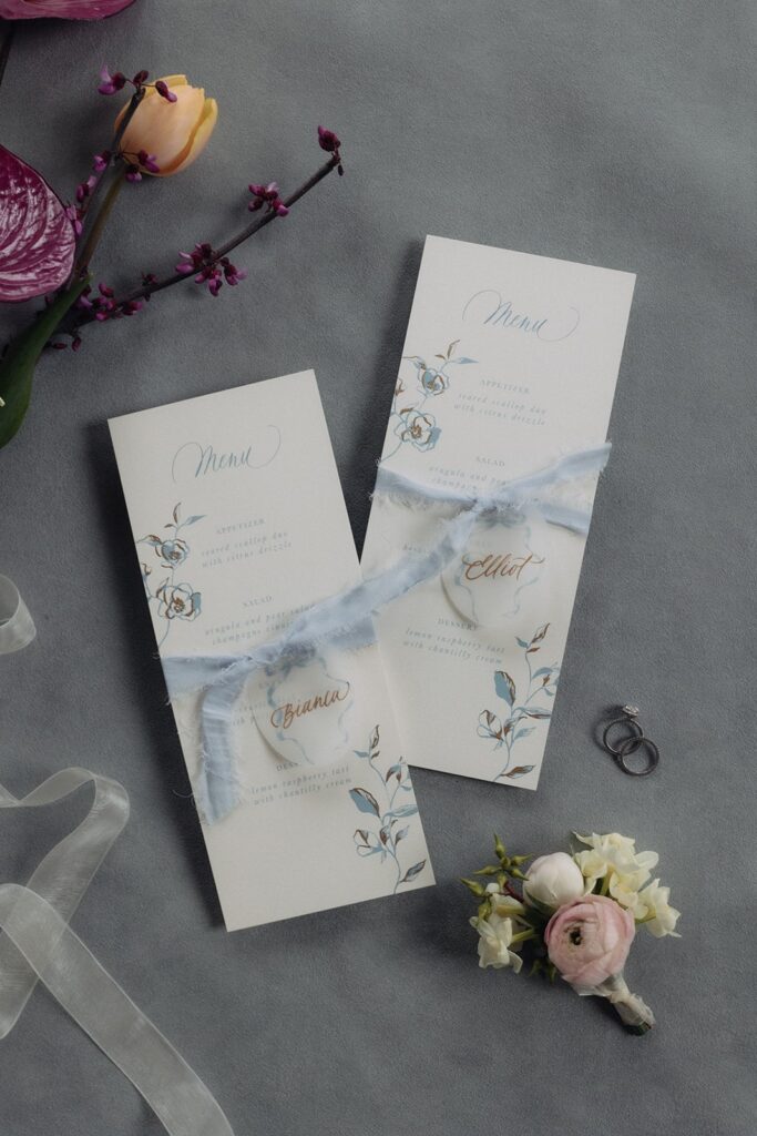 Custom blue stationery menus with calligraphy place cards tied around the menu with blue ribbon for bow themed wedding.