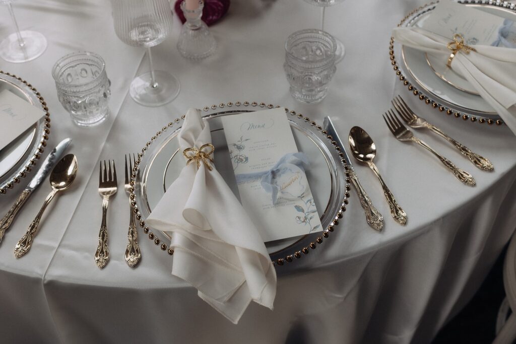 Bow themed wedding table setting with custom menu on top of french style gold and white plates.