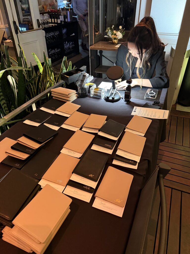 Calligraphy artist doing leather embossing on-site at a launch party with a table of completed passport covers.